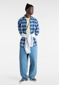 Rentoutuneita vaatteita, joihin kuuluu sininen ruudullinen flanellipaita, vihreä t-paita, harmaa huppari sidottuna vyötärölle sekä väljät farkut harmailla kengillä.