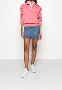 Rosa zip-up sweatshirt med vit Adidas-logga, kombinerad med en denim minikjol och vita sneakers. Avslappnad outfit med långa ärmar och krage.