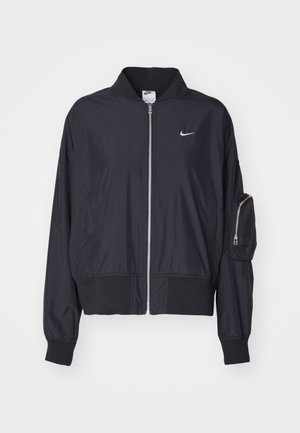 Schwarze Bomberjacke aus leichtem Material, mit einem Reißverschluss vorne, gerippten Bündchen und einer Reißverschlusstasche am Arm. Nike-Logo auf der Brust.
