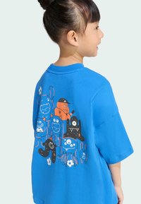 Modrá bavlnená tričko s hravými grafikami monštier v oranžovej, čiernej a modrej farbe s číslovanými dizajnmi a kvetinovým akcentom. Krátke rukávy.