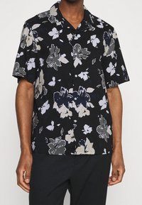 Camisa de flores negra de manga corta con grandes flores blancas y grises, cierre de botones y diseño de cuello de campamento. Fabricada con tejido ligero.