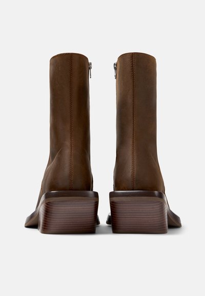 Bottines en cuir marron avec une texture lisse, un design à bout carré et un talon en bois. Caractéristiques d'une fermeture à glissière latérale.