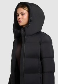 Fekete steppelt dzseki nagy kapucnival, sima textúrával, steppelt mintával és elülső cipzárral. Logó az oldalon.