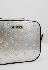 Borsa a tracolla argentata metallica con motivo logo in rilievo, rifiniture nere e ferrature dorate. Caratterizzata da una forma rettangolare e tracolla regolabile.