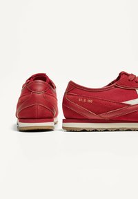Röda sneakers med en kombination av textil och läder. Slank design med vita accenter, gummisulor och en strukturerad yta. Modellnumret visas.