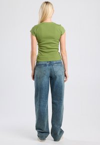 Green fitted t-shirt with cap sleeves, paired with wide-leg light blue jeans featuring faded accents and rear pocket details.