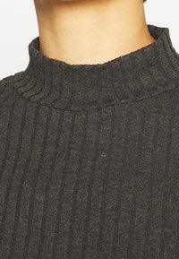 Mörkgrå ribbad polotröja med en texturerad stickning och en vikbar, hög krage. Tyget ser mjukt och figurnära ut.