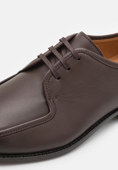 Pantofii eleganți din piele maro au un finisaj neted, un design cu șireturi și detalii de cusătură subtile de-a lungul marginilor.