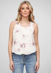 Blouse sans manches en crème avec des accents roses, dotée d'un col rond et d'un tissu doux, associée à un jean bleu taille haute.