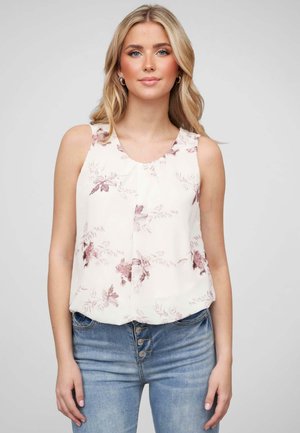 Blouse sans manches en crème avec des accents roses, dotée d'un col rond et d'un tissu doux, associée à un jean bleu taille haute.