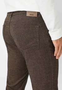 Bruine textuurbroek met een gladde afwerking, voorzien van een leren label, platte achterzakken en een recht model.