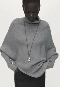 Maglione a collo alto oversize di colore grigio chiaro, realizzato in tessuto a coste; presenta una vestibilità ampia e un orlo inferiore lungo e arrotondato. Include una collana con ciondolo.