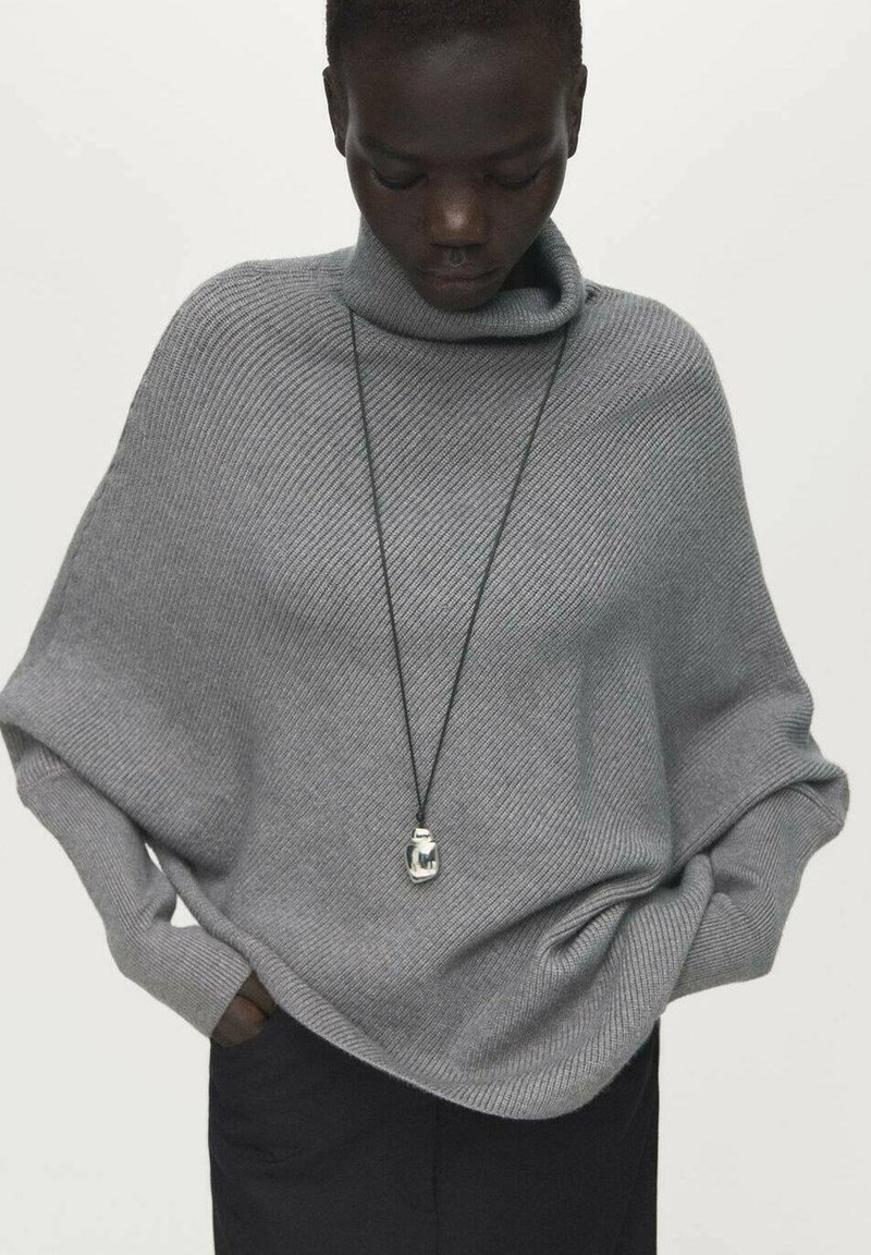 Maglione a collo alto oversize di colore grigio chiaro, realizzato in tessuto a coste; presenta una vestibilità ampia e un orlo inferiore lungo e arrotondato. Include una collana con ciondolo.