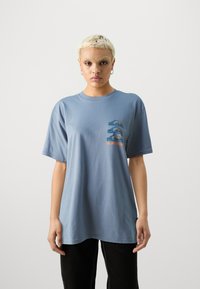 Lichtblauwe katoenen t-shirt met korte mouwen, een ronde hals en een kleine graphic print op de borst met ontwerpen van bergen en golven.