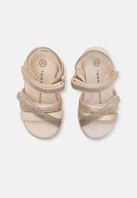 Zlaté sandály s hladkým syntetickým svrškem, pásky přes sebe s třpytivými detaily, polstrovanou stélkou a nastavitelnými zapínáními. Dostupné ve velikostech 20 a 22.