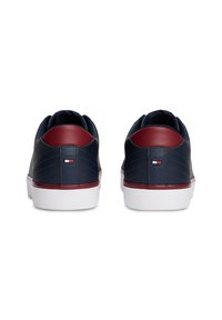 Paire de baskets basses bleu marine et rouge avec semelles blanches vues de dos, montrant un petit logo rectangulaire sur chaque talon.