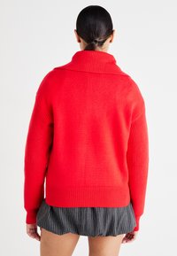 Maglione rosso a maglia con colletto alto, polsini a coste e vestibilità morbida. Tessuto testurizzato con sezioni lisce e a coste.