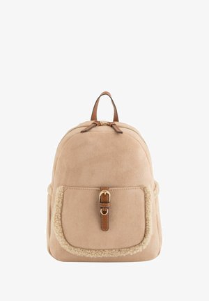 Sac à dos en daim beige avec une poignée en cuir, une fermeture éclair et une poche avant ornée d'une bordure en fourrure texturée et d'une boucle.