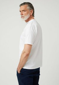 Camiseta blanca de algodón con mangas cortas, cuello redondo y un ajuste relajado. Diseño simple sin patrones o logotipos visibles.