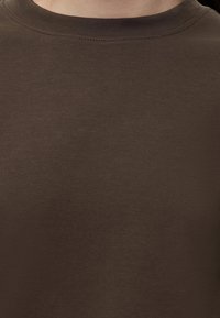 Gros plan d'une personne portant un haut en tricot marron uni à col rond.