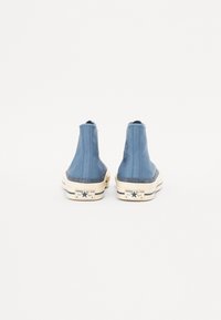 Blå kanvas ankelstøvler med høy toppdesign og hvite gummisåler som har svarte stjerner og "Converse All Star"-merkevare.