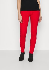 Vaqueros skinny rojos hechos de una mezcla de algodón elástico, con una textura suave y un diseño ajustado. Combinados con botas negras hasta el tobillo.