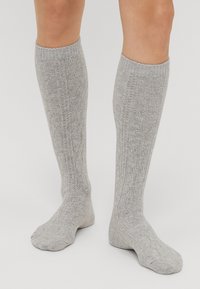 Sivé ponožky po kolená s textúrovaným vzorom, rebrovaným manžetom a mäkkým pleteným materiálom. Jednoduchý dizajn vhodný na bežné nosenie.