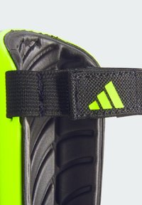 Adidas shin guard features a bright neon yellow shell with a textured black strap. It includes a molded design for enhanced protection.