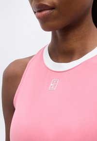 Κοντινό πλάνο ενός ατόμου που φοράει ροζ μπλουζάκι χωρίς μανίκια με λευκή διακόσμηση και μικρό λευκό λογότυπο Nike στο στήθος.