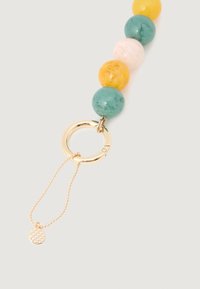Chaveiro com grandes contas redondas em verde, amarelo e branco, preso a um anel dourado com um pequeno pendant texturizado numa corrente.