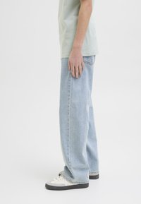Ljusblå, löst sittande jeans med rak ben, tillverkade av denim, parat med vita och grå sneakers, mot en enfärgad bakgrund.