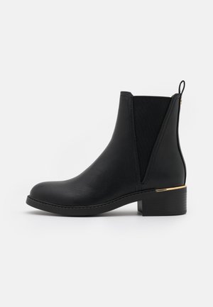 Bottine noire en cuir lisse avec des panneaux latéraux élastiques et un accent doré sur le talon. Talon bloc qui offre de la stabilité.