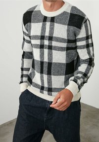 Suéter de punto a rayas negro y blanco con cuello redondo, puños y dobladillo acanalados. Llevado sobre pantalones de mezclilla oscuros.