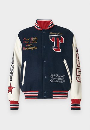 Chaqueta varsity en azul marino y crema con acentos rojos, que presenta texto bordado, un logo de "T" y un cuello y puños de canalé a rayas.