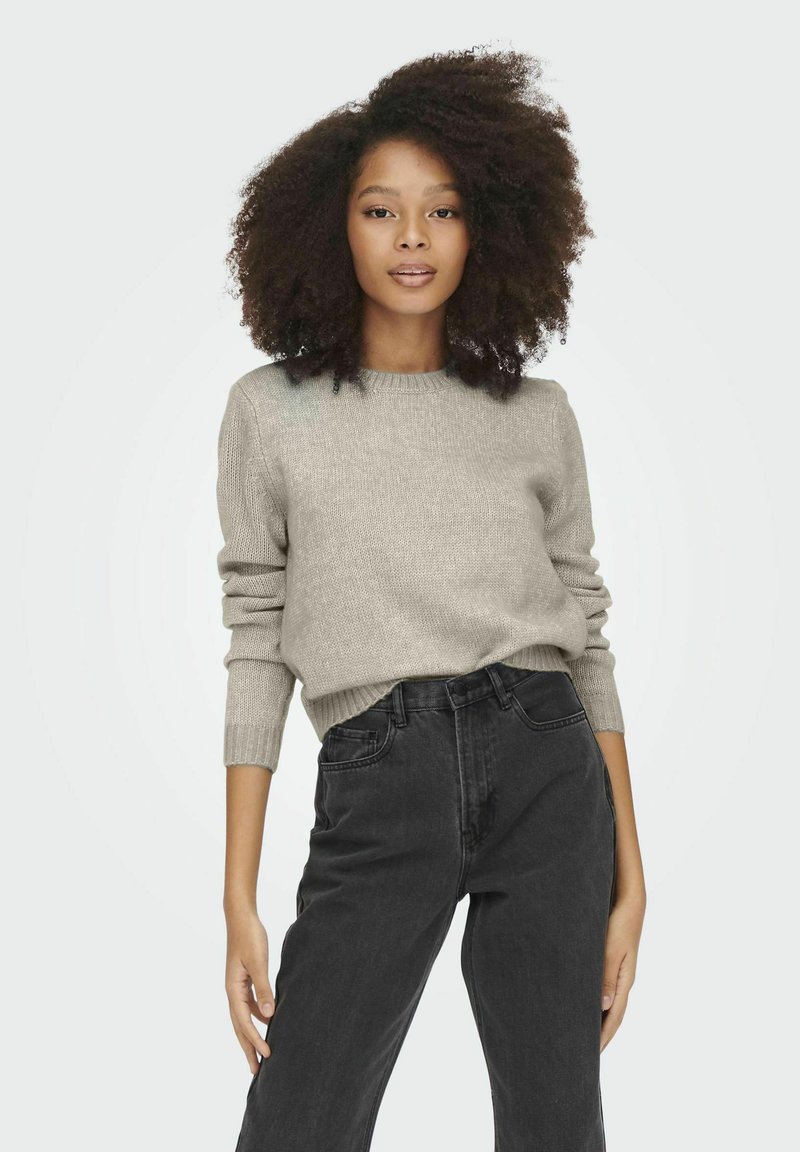Lichtgrijs gebreid sweater met geribbelde manchetten en een ronde halslijn, gecombineerd met high-waisted zwarte jeans. Zachte textuur en eenvoudig ontwerp.