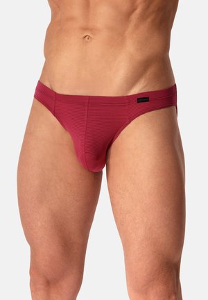 Mannelijke torso en bovenbenen gekleed in strakke rode slip met subtiele horizontale strepen en een klein zwart label op de tailleband.