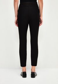Zwarte strakke broek met een brede tailleband, gemaakt van rekbare stof. Het ontwerp heeft een slanke pijp en een enkellange snit.