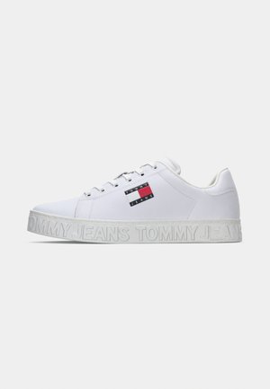Witte lage sneaker met veters, voorzien van een Tommy Jeans logo patch aan de zijkant en gegraveerde "Tommy Jeans" branding op de zool.