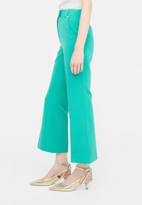Tyrkysové široké nohavice s vysokým pásom, vyrobené z hladkej látky. Spojené so zlatými slingback topánkami s špicatou špičkou a nízkym podpätkom.