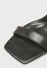 Sandale en cuir noir avec un bout carré et une large bride unique à l'avant.