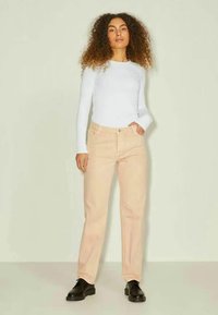 Calças de ganga rosa claro com corte reto, cinco bolsos e passadores de cinto, combinadas com uma blusa de mangas longas branca e sapatos pretos.