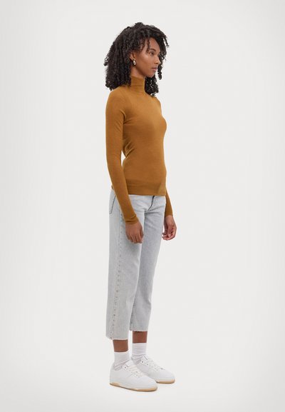 Maglione a maniche lunghe slim-fit con collo a imbuto in marrone, abbinato a jeans cropped blu chiaro e sneakers bianche. Presenta una texture liscia e una silhouette aderente.