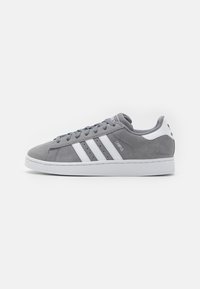 Sneaker Adidas Campus in suede grigio con strisce bianche, lacci abbinati e suola bianca su uno sfondo chiaro e semplice.