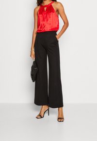 Haut en satin rouge avec détail en trou de serrure, associé à un pantalon large noir et des talons aiguilles noirs. Comprend un sac à main noir fluffy.