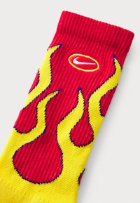 Piros és sárga zokni lángmintákkal, bordázott textúrával, és egy kicsi sárga Nike logóval piros háttérrel.