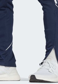 Marineblaues Trainingsteil mit Seiteneingängen und weißen Akzentnähten, kombiniert mit weißen Sportschuhen, die ein strukturiertes Mesh-Obermaterial und dicke Sohlen aufweisen.