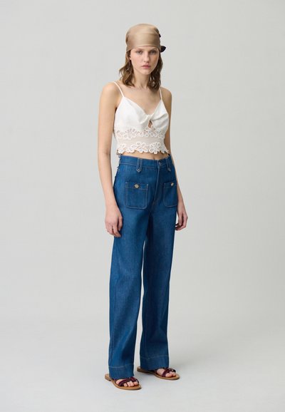 Crop top en satin blanc avec des bordures en dentelle et une ouverture en forme de clé, associé à un pantalon large en denim bleu taille haute avec des poches avant.