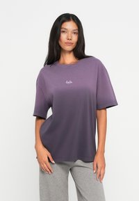 Brīvi pieguļoša purpura t-krekla ar mīkstu audumu, ar īsām piedurknēm un apaļu kakla izgriezumu. Neliels balts logotips ir centrēts uz krūtīm.