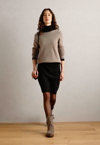 Brown knit sweater, black skirt, and beige ankle boots. The outfit features a relaxed fit and smooth textures, with minimal embellishments.