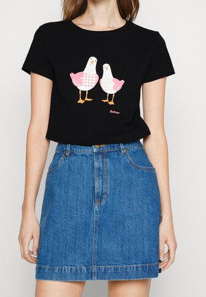 Černé tričko s dvěma ilustracemi racek v růžové a bílé barvě nad modrou džínovou sukní, kterou nosí osoba s světlou pokožkou.